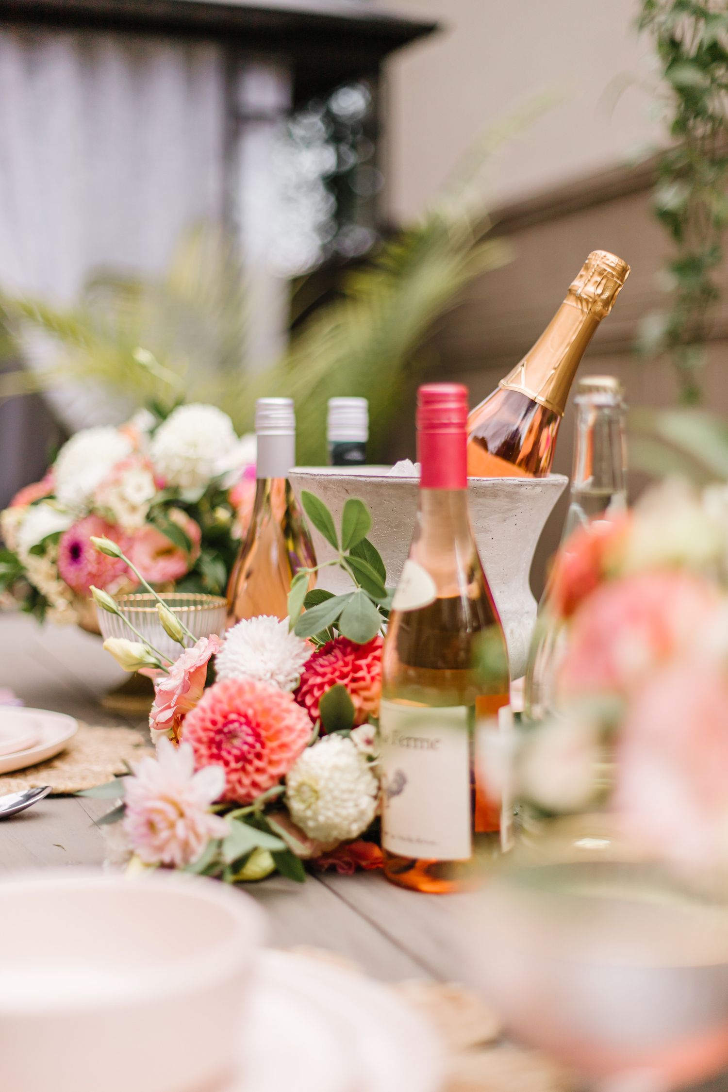 Elegant table setting with pink flowers, champagne bottles and delicate glassware.