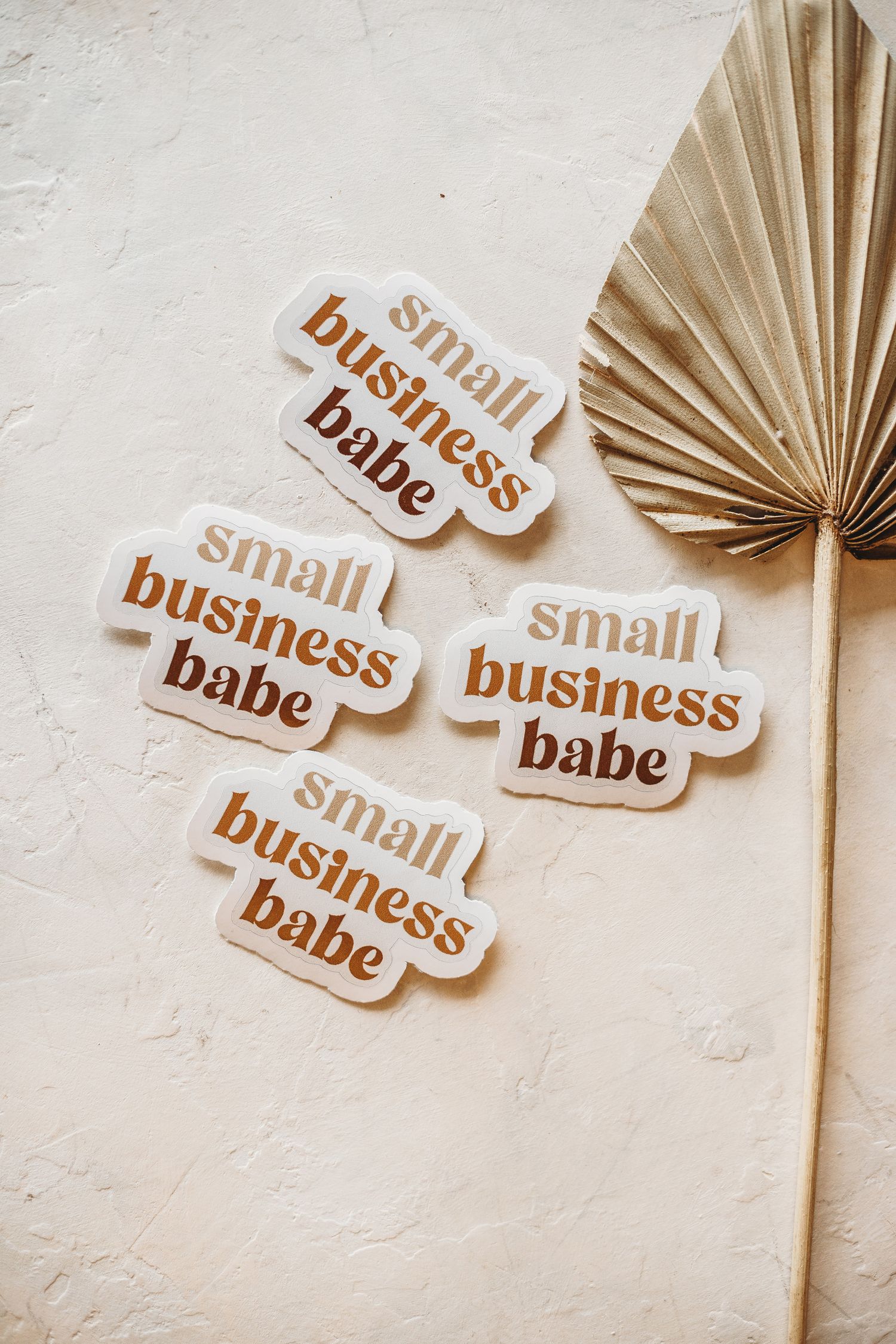 Brown stickers with 'small business babe' text arranged on textured white surface.