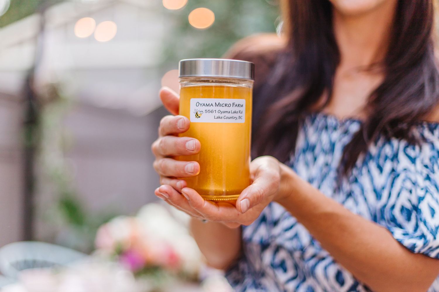 A golden-colored beverage in a glass being held against a floral background.
