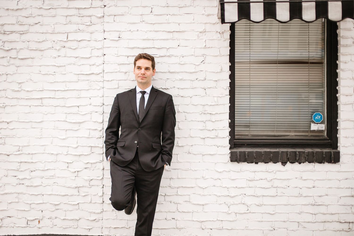 Business professional poses confidently against white brick wall exterior.