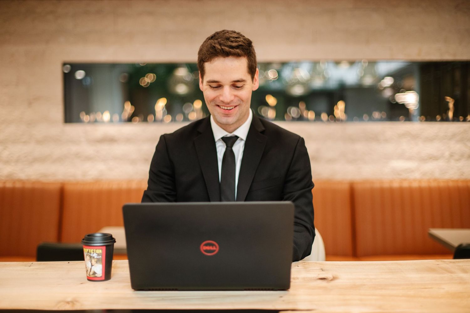 Business professional working on laptop in modern restaurant setting with warm lighting.