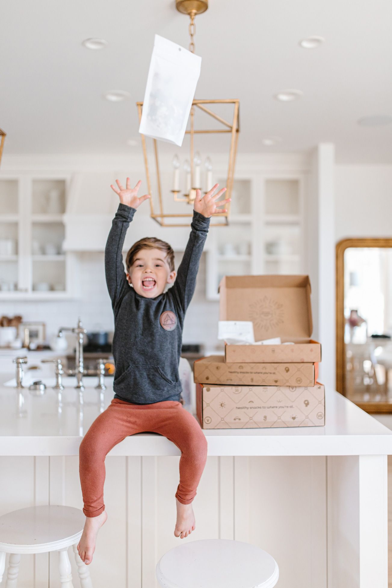 Energetic child jumping on kitchen counter while holding white paper in bright modern kitchen.