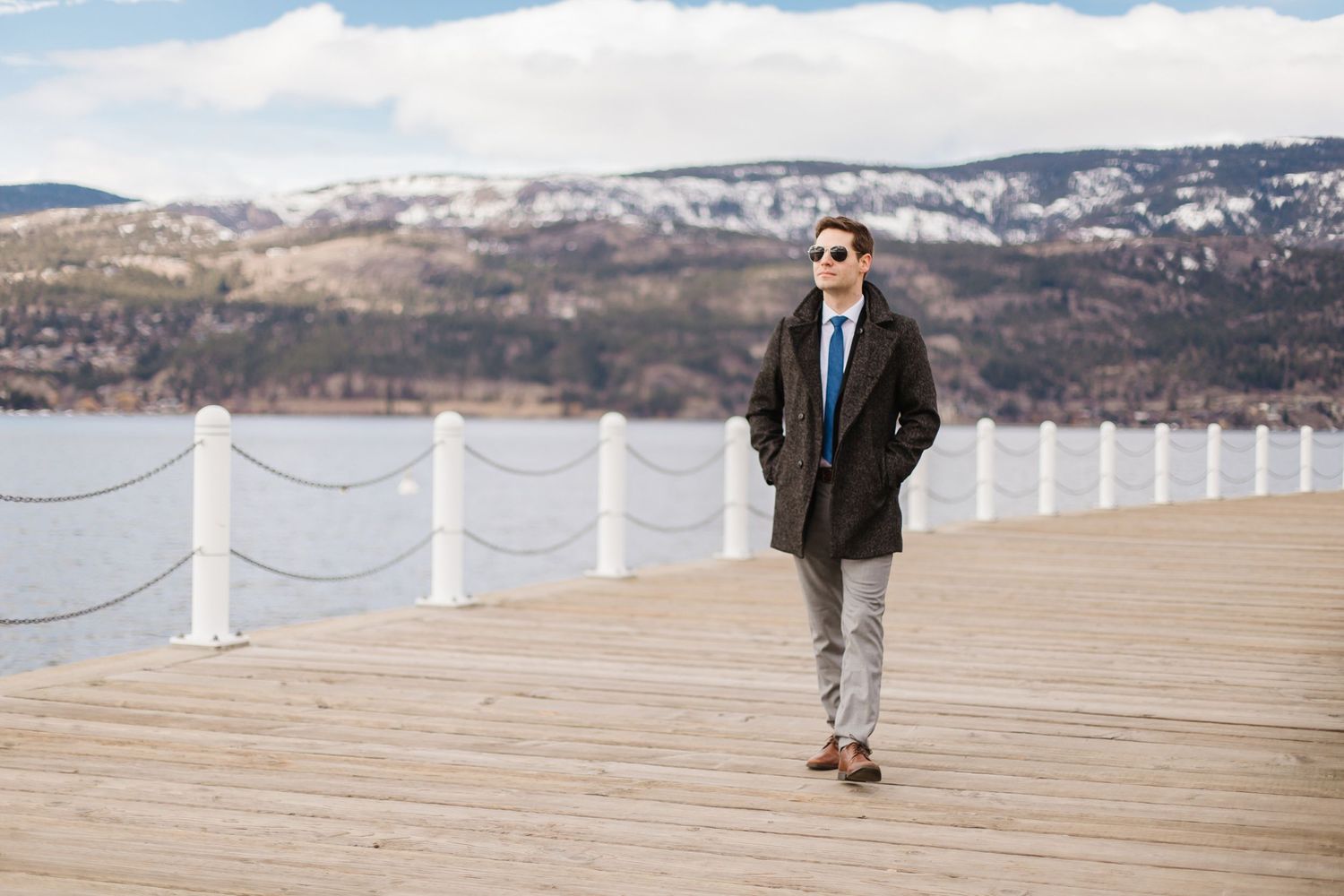 Business professional walking along waterfront boardwalk with mountain and lake views.