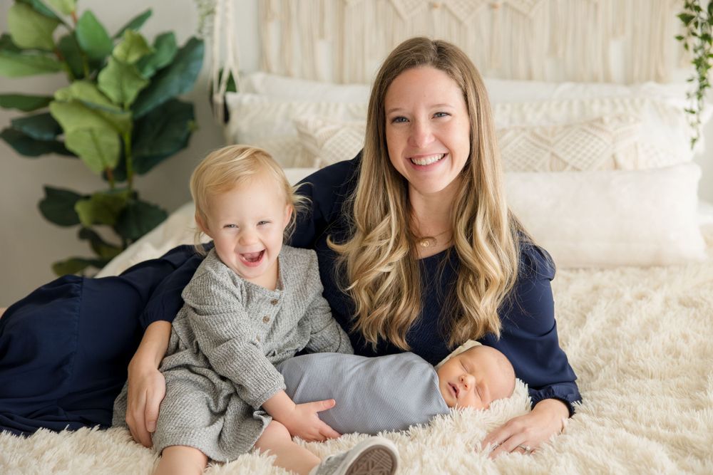 Joyful family moment captured on white bedding with boho wall decor and greenery.
