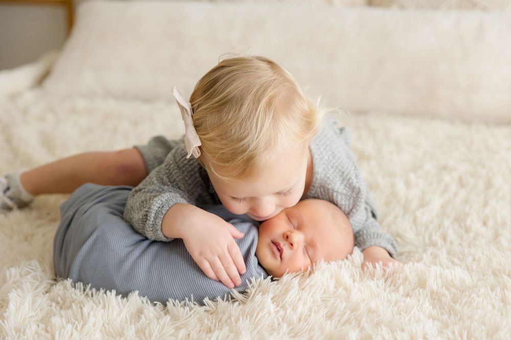 Siblings bonding together on white fluffy rug.