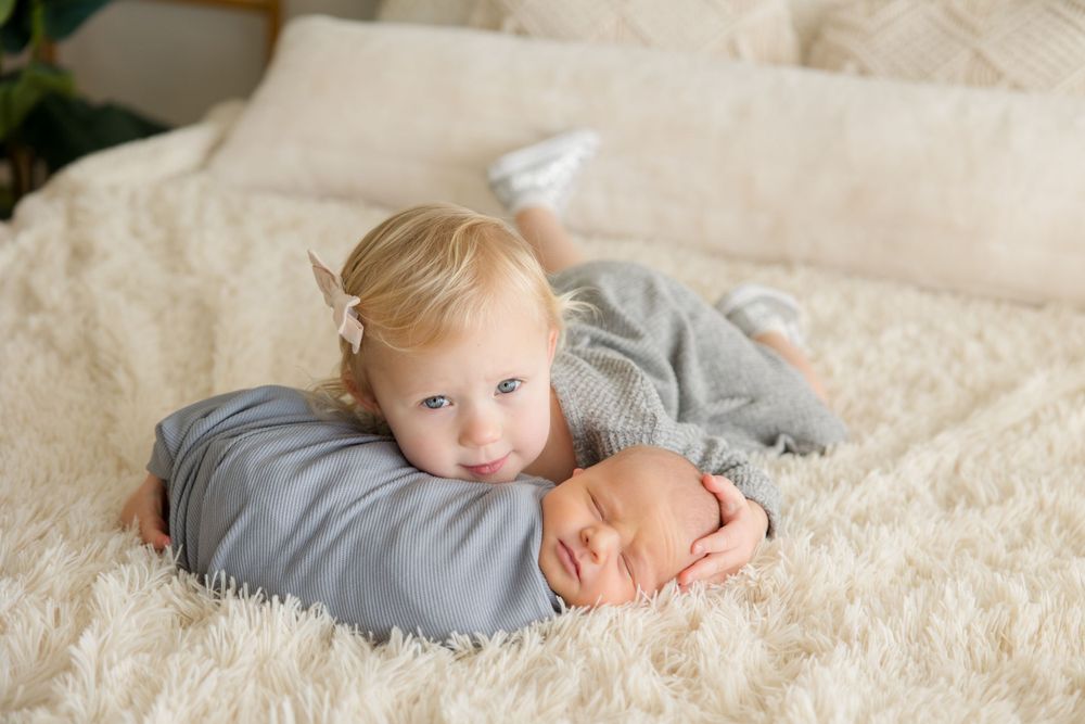 Sweet siblings cuddling on cream colored bedding.