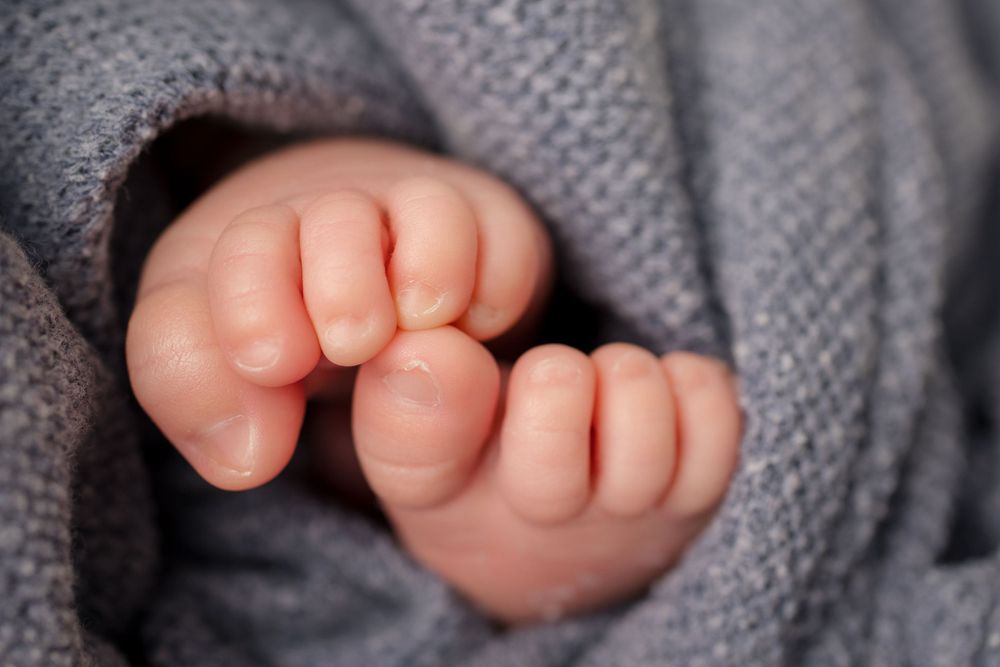 Macro shot of newborn baby toes peeking through gray knit blanket.