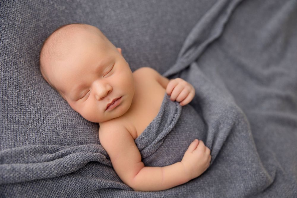 Sleeping infant wrapped in cozy gray blanket during professional photo session.