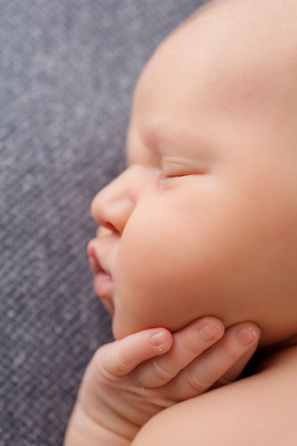 Side profile of sleeping newborn with hand gently supporting face.