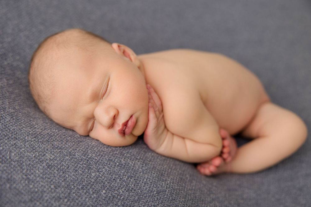 Peaceful sleeping newborn baby curled up on soft gray fabric in natural light.