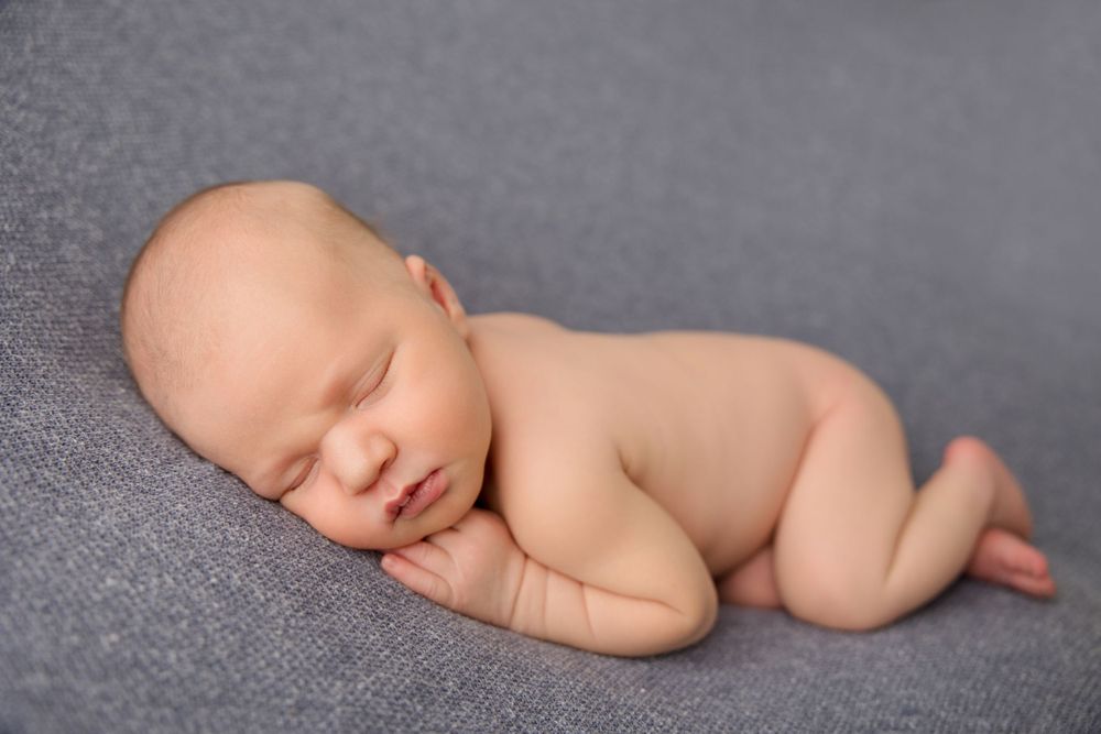 Peaceful sleeping newborn baby curled up on gray textile background.