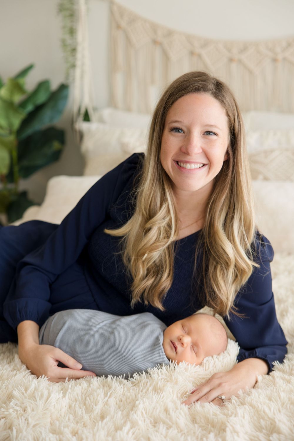 Professional portrait on white fluffy bedding with soft macrame backdrop and green plants in the background.