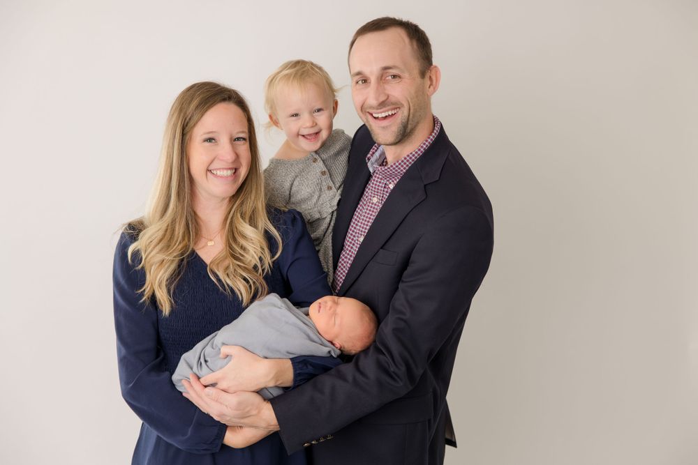 Family studio portrait against neutral background in coordinated navy and burgundy outfits.