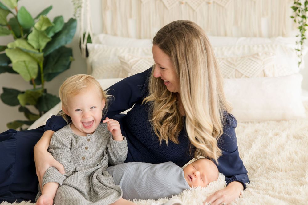 Family portrait on cream bedding with decorative macrame wall hanging and potted plants.