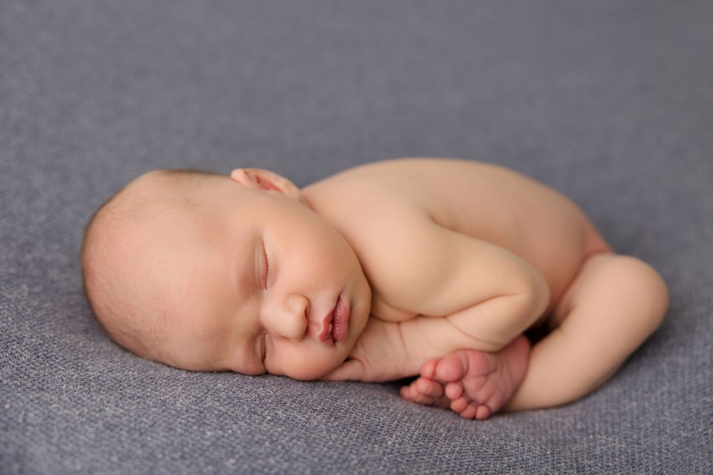 Sleeping newborn in fetal position on soft gray backdrop.