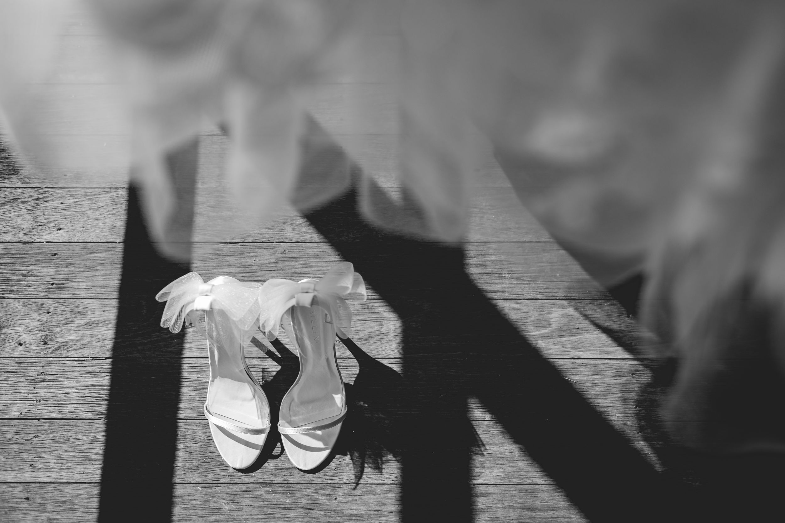 Wedding shoes photographed with dramatic shadows on wooden floor.