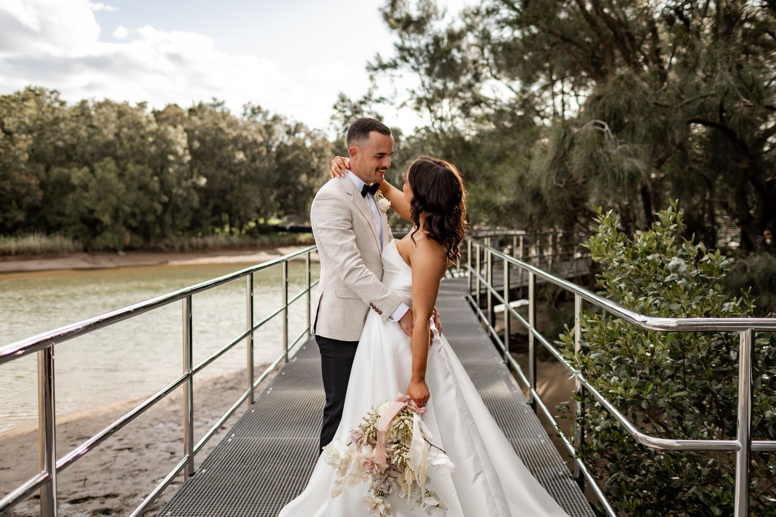 Romantic wedding portrait on a bridge overlooking water during golden hour.