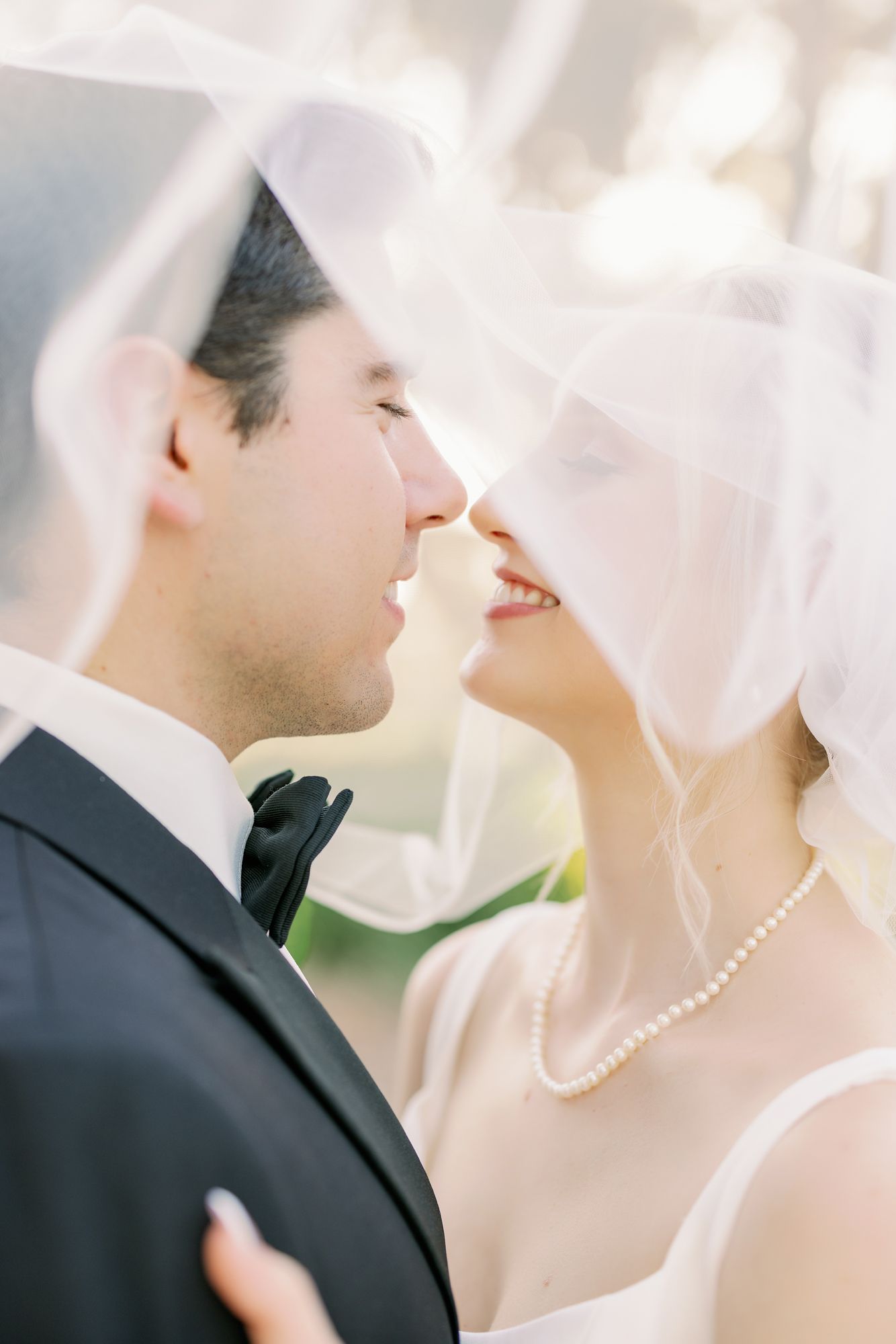 Tender wedding moment captured through delicate veil in soft natural lighting.