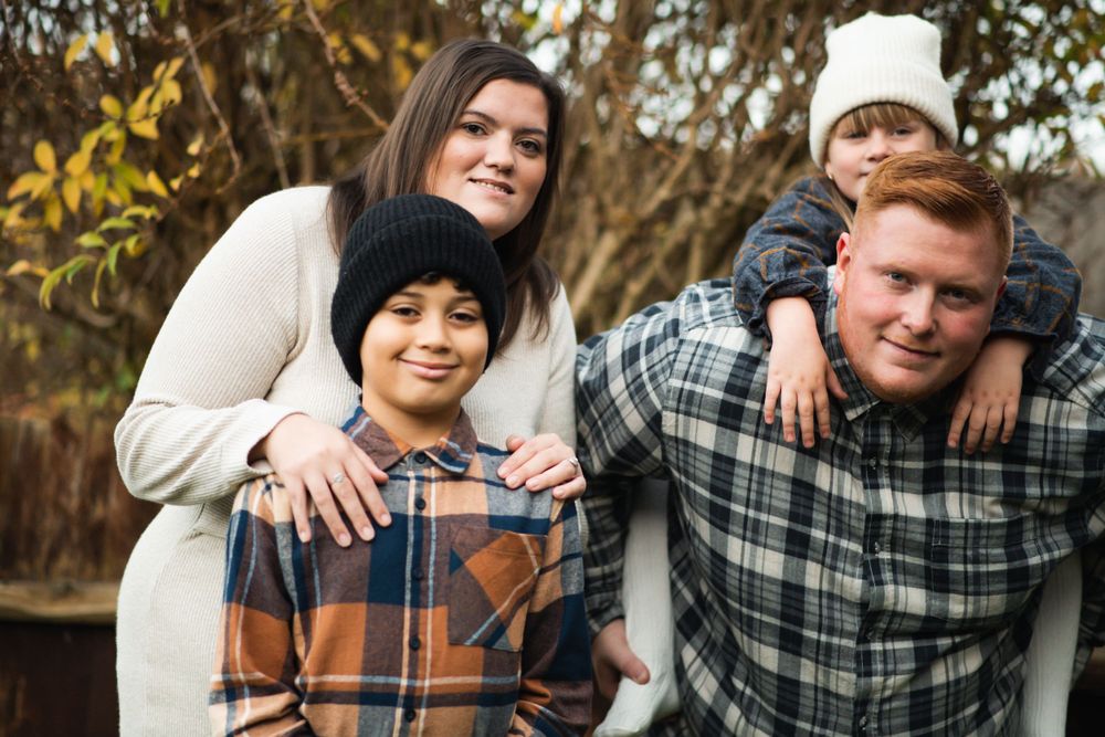 Family portrait with coordinating plaid shirts against natural backdrop.