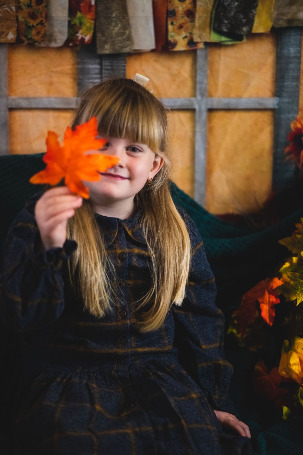 Young person in dark dress holding autumn leaf with seasonal decorations.