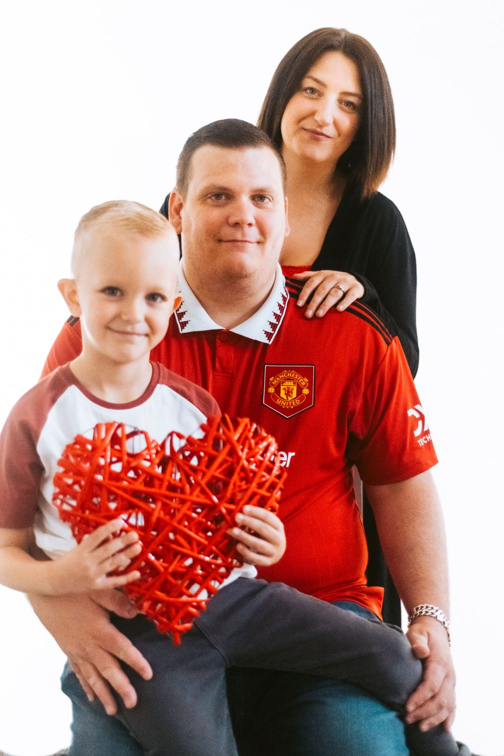 Family portrait with red heart prop and Manchester United soccer jersey.