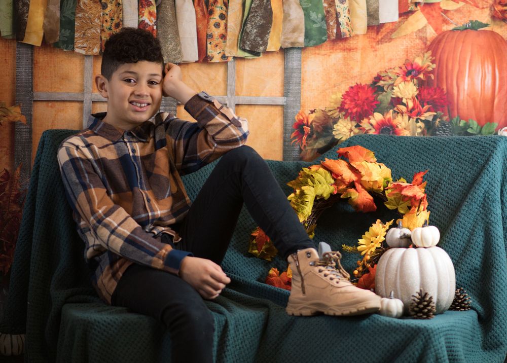 Smiling person in plaid sitting on teal couch with autumn decorations and pumpkins.