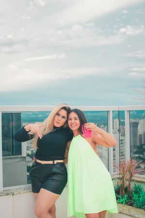 Two people pose casually on a bright rooftop terrace with modern buildings in the background.