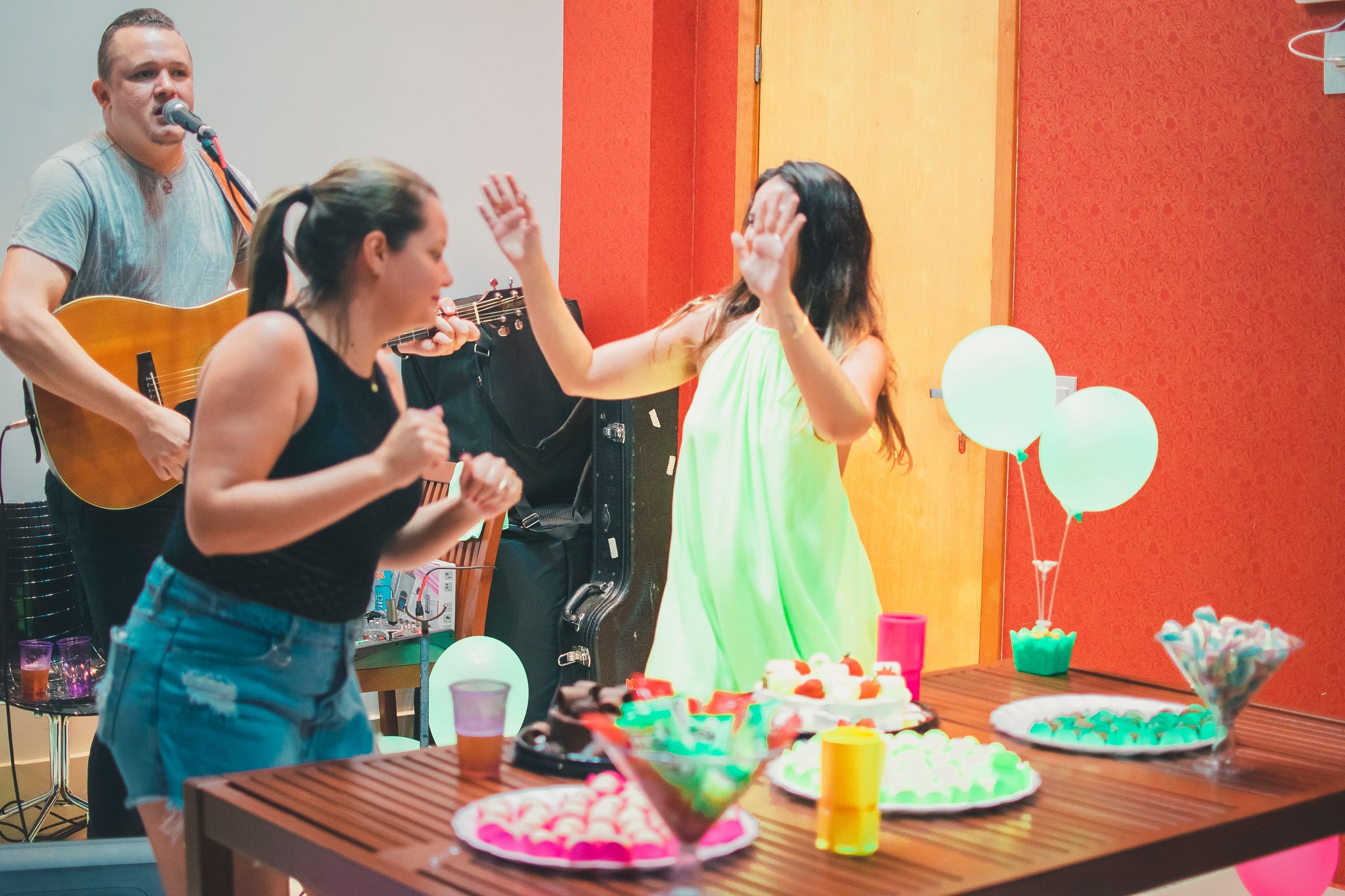 Party scene with people enjoying drinks and conversation against an orange wall backdrop.