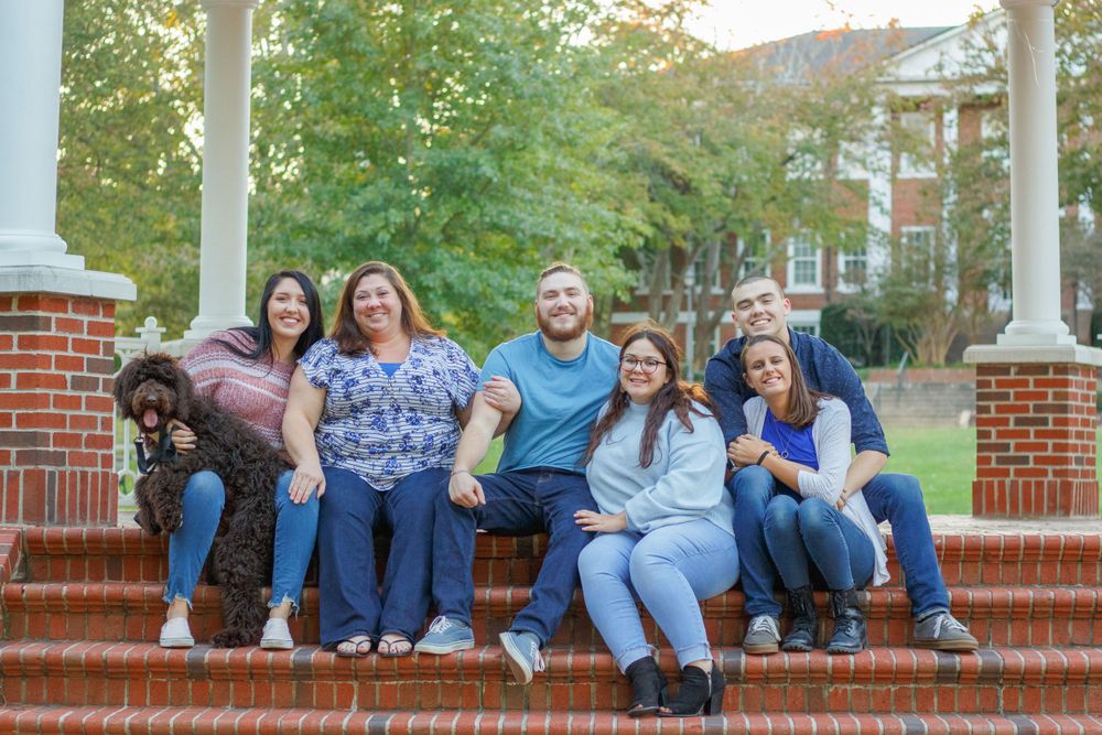 Group of people sitting together on brick steps with white columns and fall foliage in background.