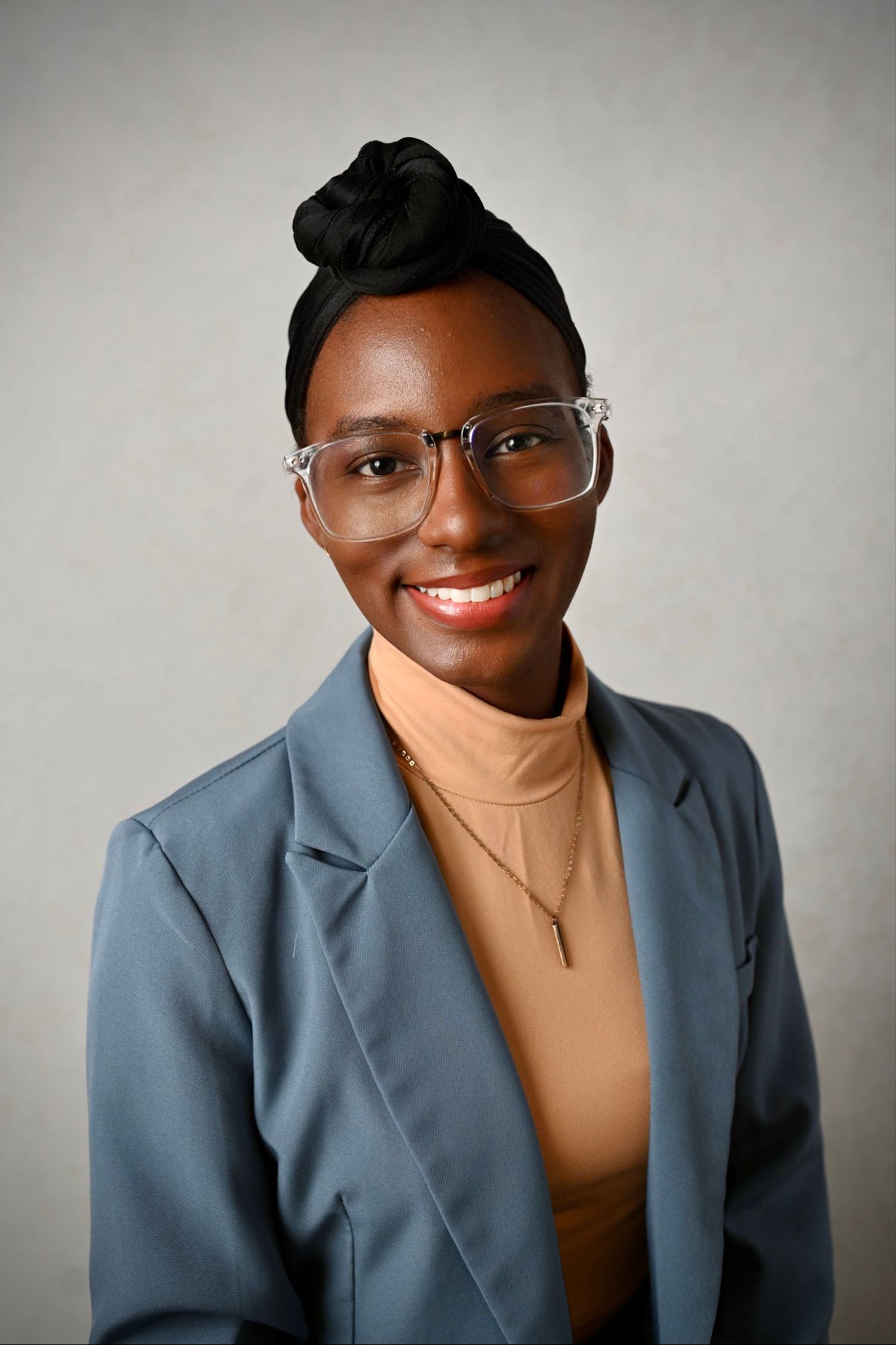 Professional headshot of person in glasses wearing blue blazer and tan turtleneck.