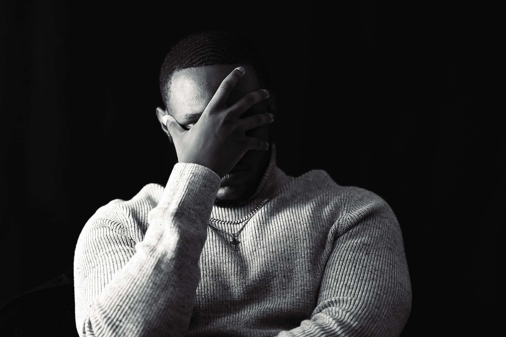 Person in dramatic black and white lighting wearing turtleneck sweater shows contemplative expression.