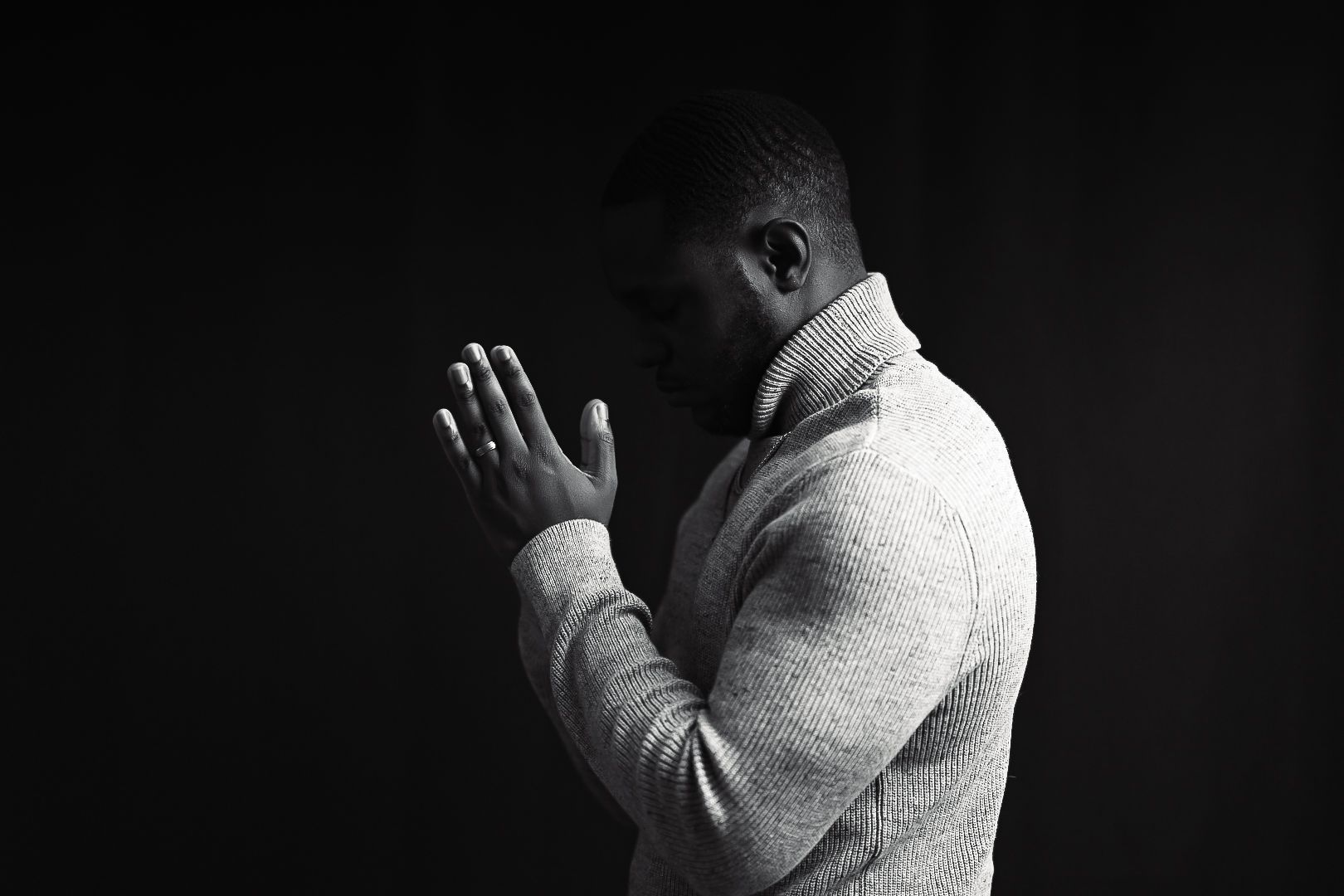 Figure in beige turtleneck sweater photographed against dark background in moody lighting.