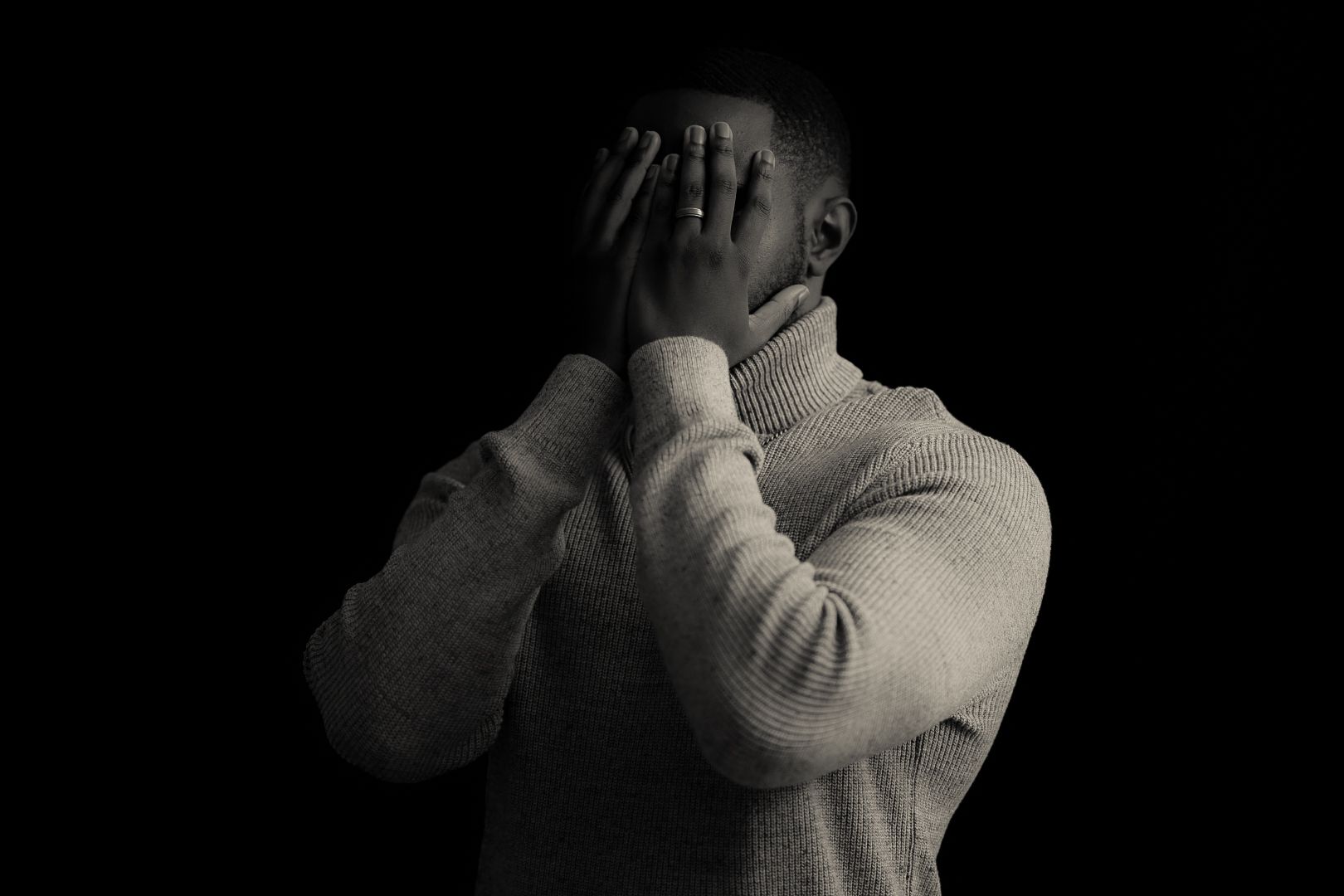 Dramatic portrait of person in light colored sweater against black background.