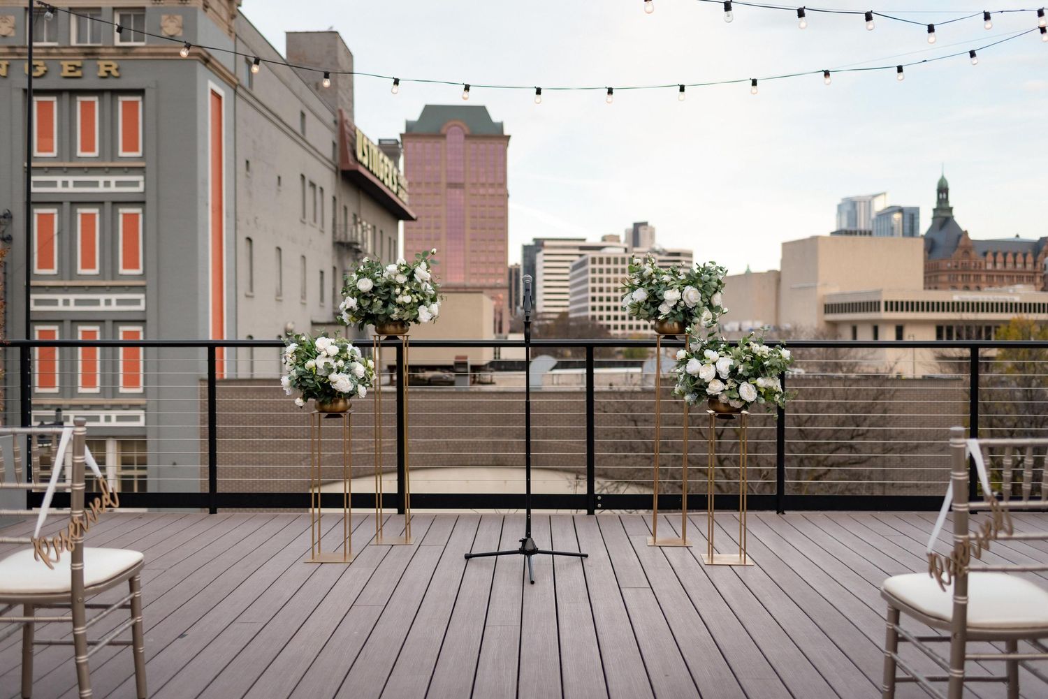 Urban rooftop terrace with string lights and floral arrangements between two chairs overlooking city buildings.