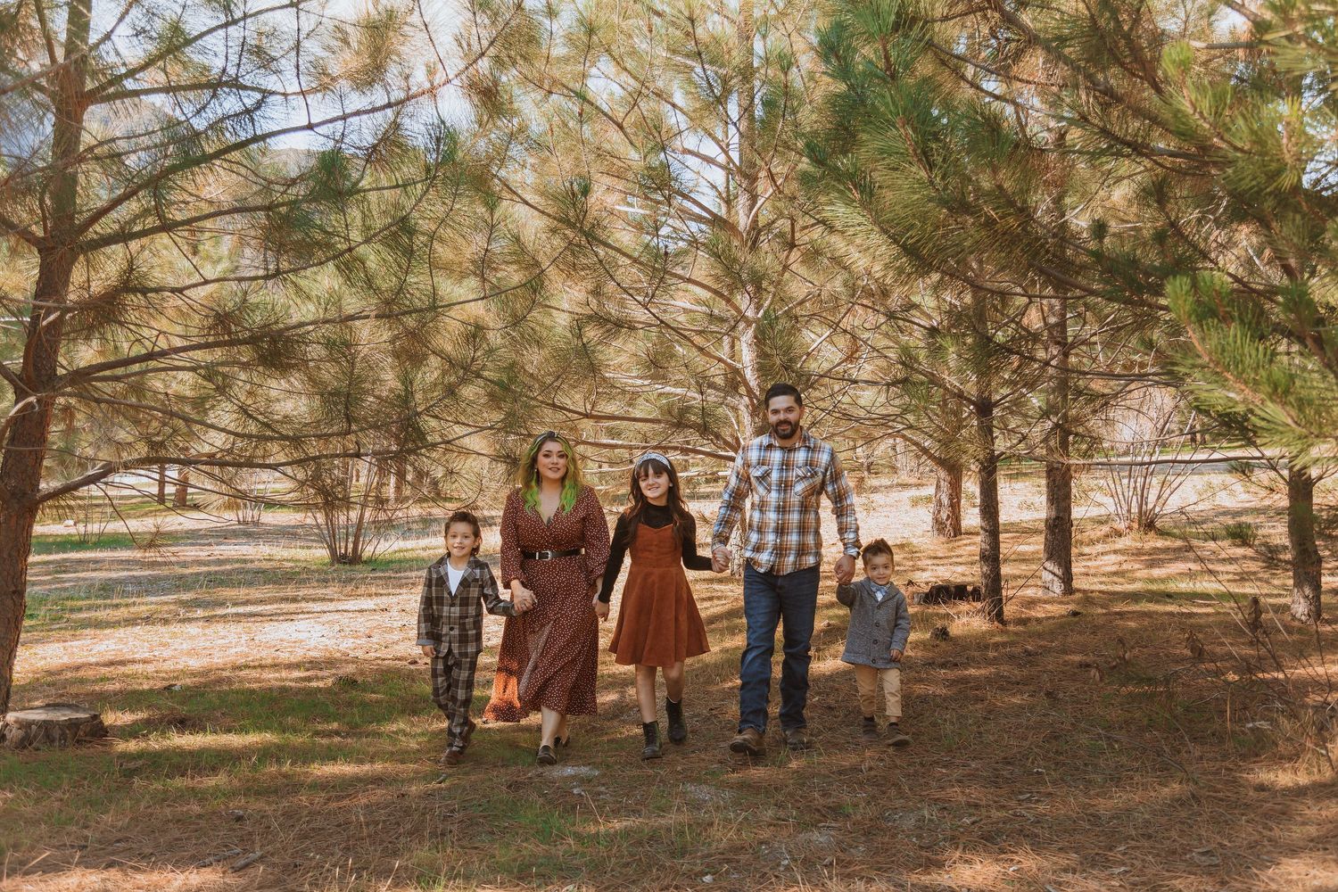 Family walking together through pine trees on sunny autumn day.