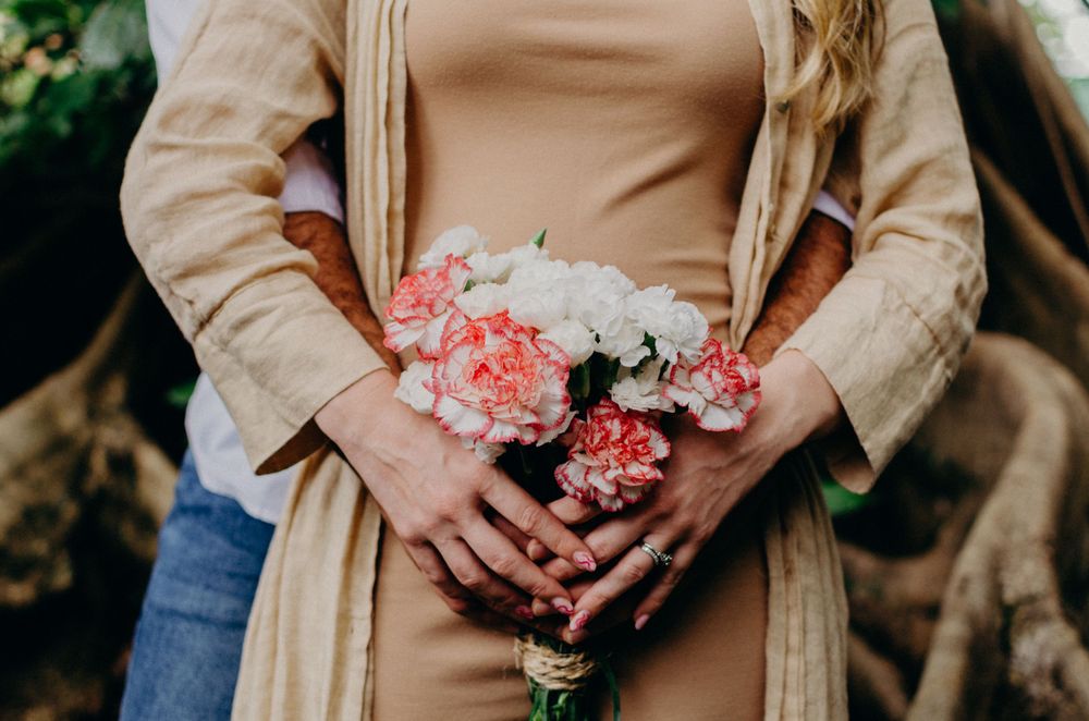 Close-up of hands holding pink and white carnations against a beige dress.