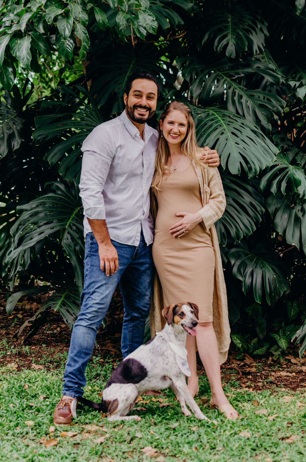 Couple with their dog posing together against lush tropical foliage.