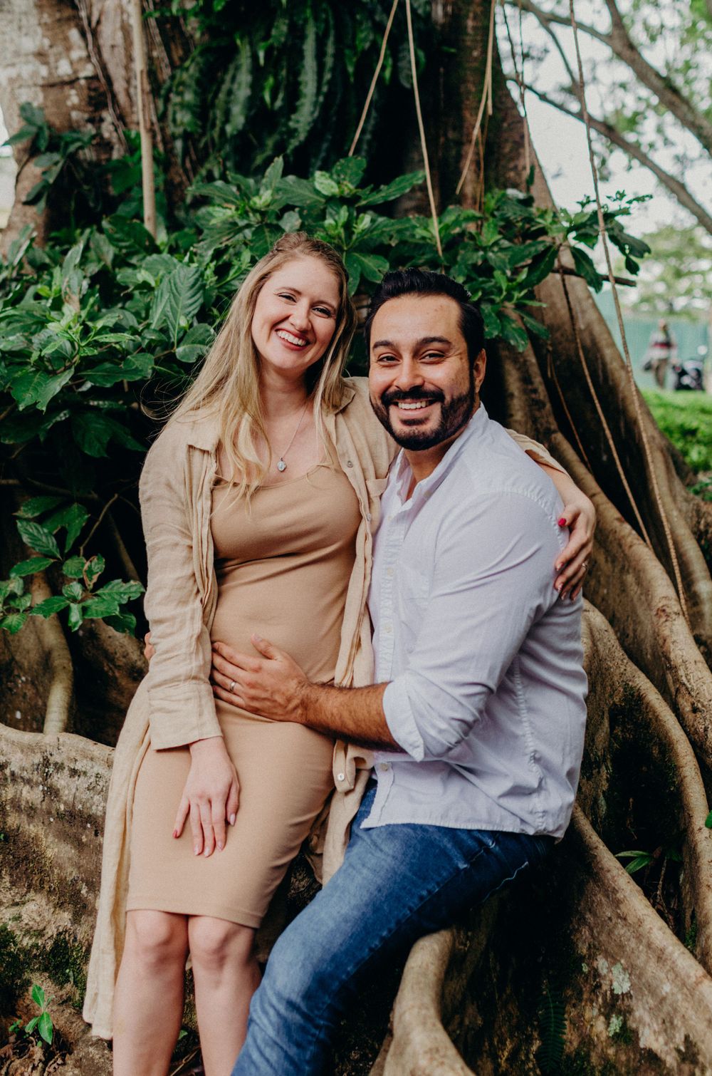 Couple posing together by a large tree root system in a garden setting.