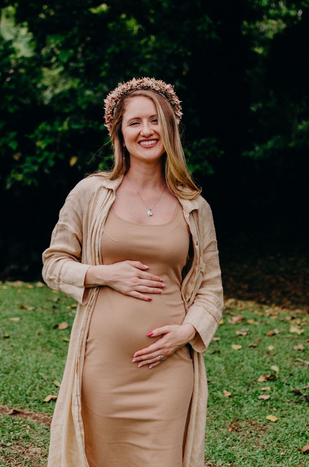 Beautiful maternity portrait in neutral tones with a floral crown against green foliage.