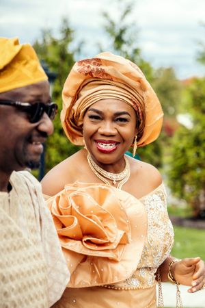 Wedding guest in traditional African attire and headwrap at outdoor celebration.