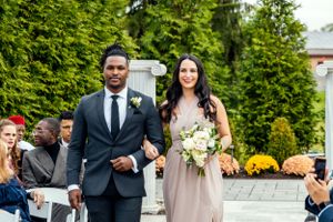 A couple walking down the aisle with coordinated blush pink and gray attire at an outdoor wedding ceremony.