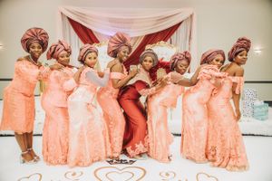 Wedding party members in peach dresses and matching headwraps pose together against a draped backdrop.