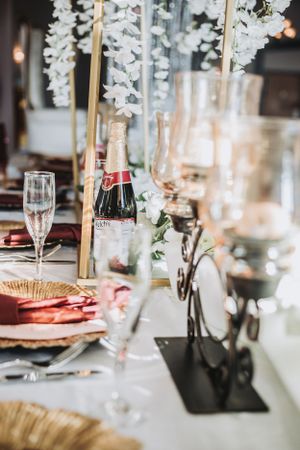 Elegant wedding reception table setting with champagne bottle and hanging white floral decorations.