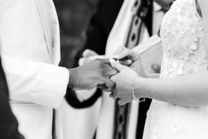 Black and white close-up of hands exchanging rings during wedding ceremony.
