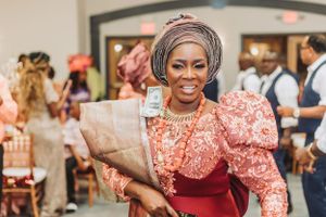 Wedding guest in a coral patterned dress with puff sleeves and headwrap carries a gift bag.