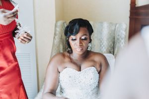 A bride in an elegant white beaded strapless wedding gown sits in preparation for her special day.