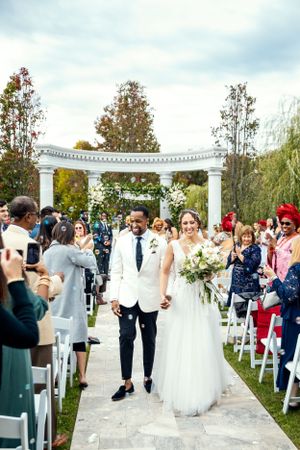 Garden wedding ceremony under white pergola with floral arrangements and seated guests.