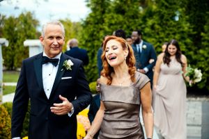 A father and daughter share a joyful moment walking down the aisle at a formal wedding.