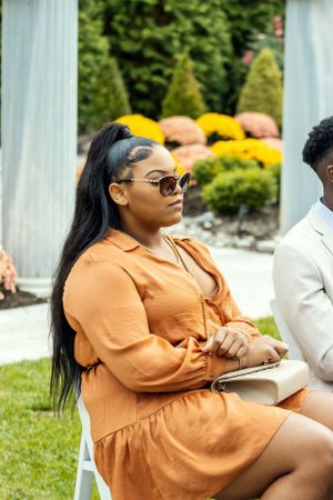 Guest in orange dress seated at outdoor wedding venue with garden backdrop.