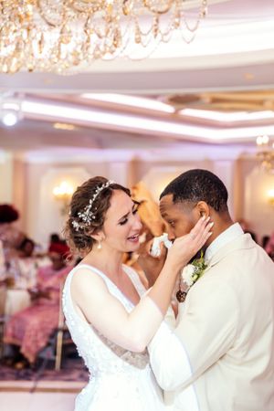 A tender moment between newlyweds in a luxurious ballroom with crystal chandeliers overhead.